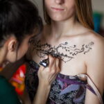 Séance de tatouage au henné sur le décolleté, avec motifs floraux complexes en cours de création.