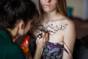 Séance de tatouage au henné sur le décolleté, avec motifs floraux complexes en cours de création.