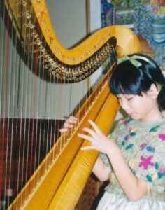 Une jeune fille, identifiée comme la jeune Eru Gibson, joue avec concentration d'une grande harpe classique en bois clair.