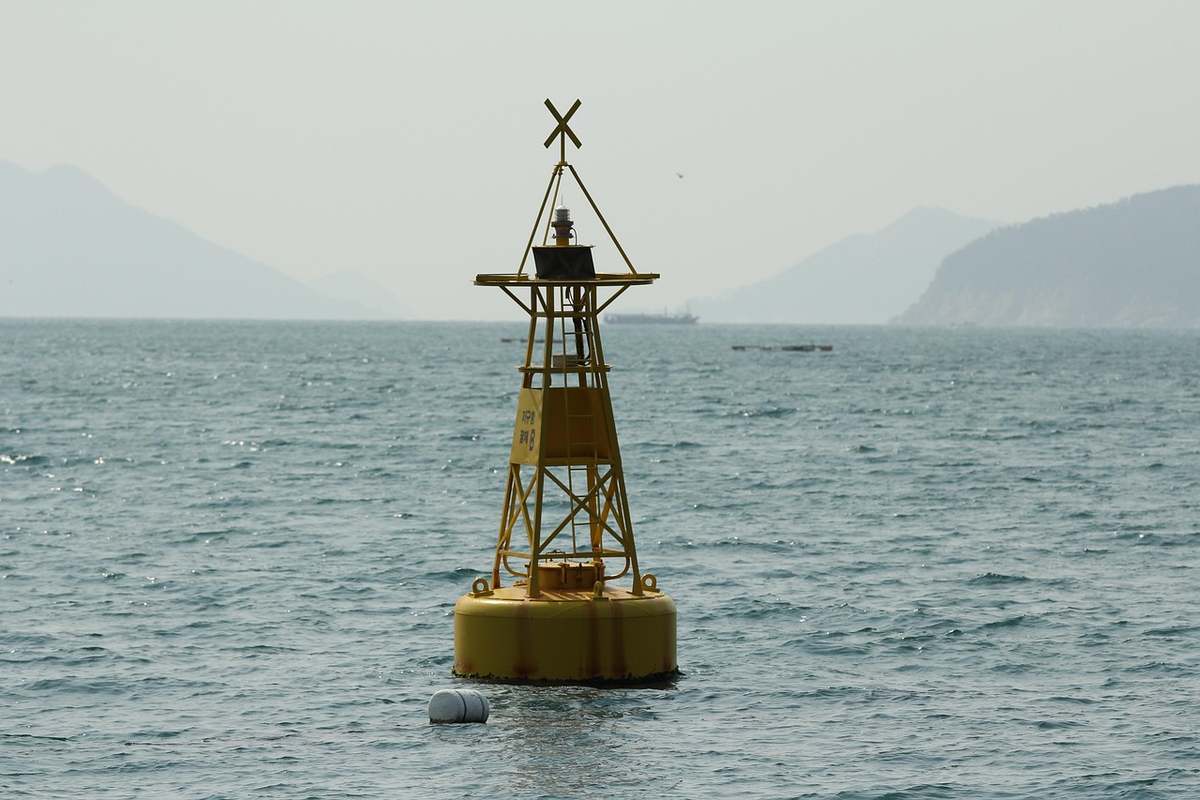 Balise jaune flottante sur la mer avec un mât triangulaire surmonté d'une croix, montagnes lointaines Balise jaune flottante sur la mer avec un mât triangulaire surmonté d'une croix, montagnes lointaines