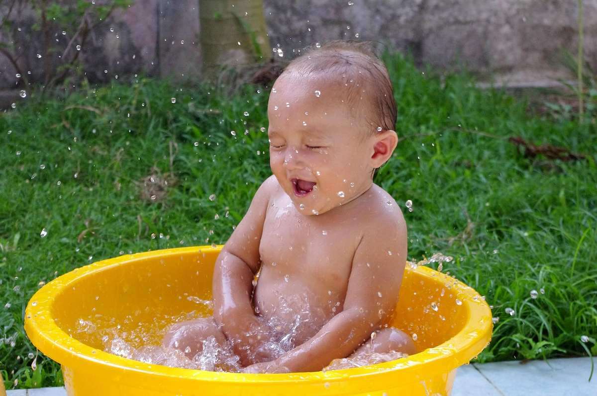 Un bébé s'amuse en éclaboussant l'eau dans un seau jaune Un bébé s'amuse en éclaboussant l'eau dans un seau jaune